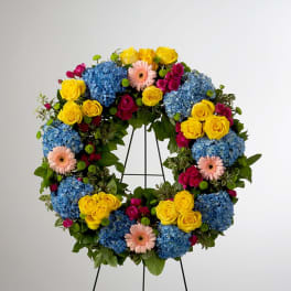 Colorful standing wreath with blue hydrangeas, yellow roses, and pink gerbera daisies on an easel