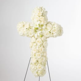 Standing cross-shaped spray of white roses, lilies, and hydrangeas on a metal easel.