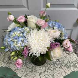 Pastel bouquet with blue hydrangeas, white chrysanthemum, and pink roses in a glass vase.