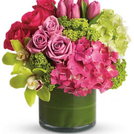 Pink roses, tulips, hydrangea, and orchids in a green glass vase