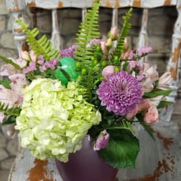 Mixed bouquet with green hydrangea and purple blooms in a mauve vase on a rustic chair.