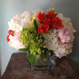 Bouquet of red roses, white hydrangeas, and pink peonies in a square glass vase