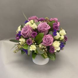 Lavender roses and purple flowers arranged in a white vase