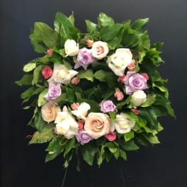 Circular wreath of pastel roses and greenery on a dark stand