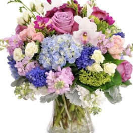 Pastel bouquet of roses, hydrangeas, orchids and mixed blooms arranged in a clear glass vase