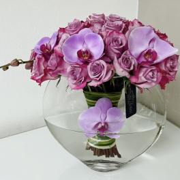 Pink roses and lavender orchids arranged in a clear glass vase