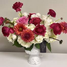 Pink and white flower arrangement in a white pedestal vase