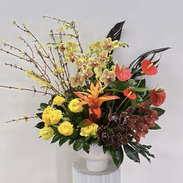Tropical floral arrangement with orchids, anthuriums, and yellow roses in a white vase
