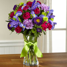 Bouquet of purple, pink, and green flowers in a glass vase with a ribbon