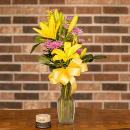 Yellow lilies and pink flowers in a glass vase with a yellow ribbon
