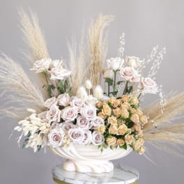 Wide arrangement of blush and peach roses with pampas grass in a cream pedestal bowl