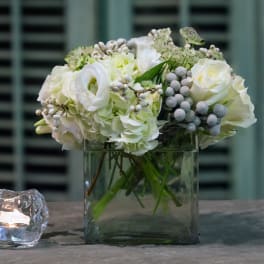 White floral arrangement in a square glass vase beside a candle holder