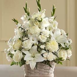 White floral arrangement in a woven basket with lilies and roses