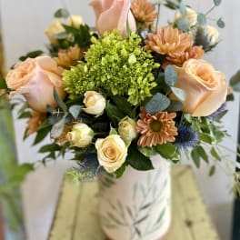 Peach roses and orange daisies in a patterned vase