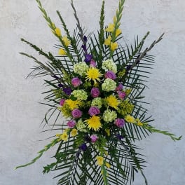 Standing floral spray with purple roses, yellow blooms, and palm fronds