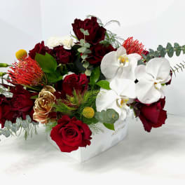 Red roses and white orchids arranged in a white box