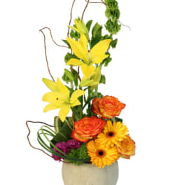 Tall mixed flower arrangement in a beige vase with yellow lilies and orange roses
