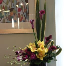 Tall floral arrangement with yellow orchids and purple calla lilies in a black vase