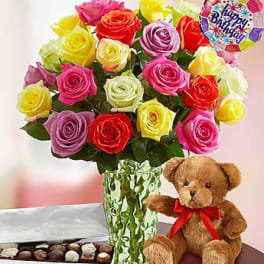 Colorful rose bouquet in a glass vase with a teddy bear, chocolates, and a birthday balloon