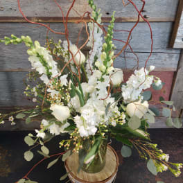 White floral arrangement in a glass vase with curly branches