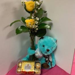 Yellow roses in a glass vase with a blue teddy bear and chocolates