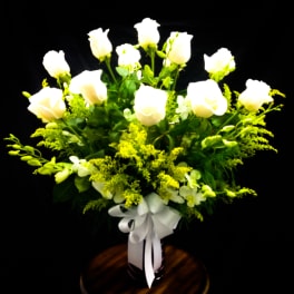 White roses arranged in a vase with yellow filler flowers and a white ribbon