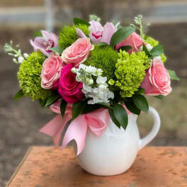 Pink roses and green blooms arranged in a white pitcher vase