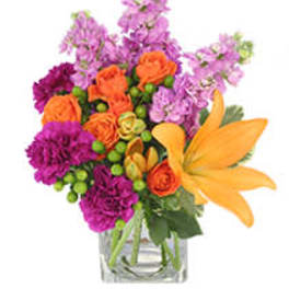 Orange lilies and purple flowers in a clear glass vase