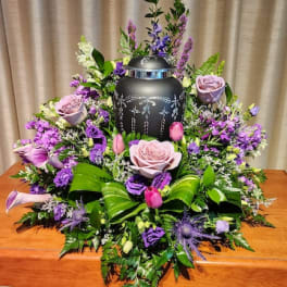 Purple floral arrangement around a black urn on a table