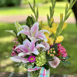 Bouquet of pink lilies and yellow flowers in a glass vase with a plaid ribbon