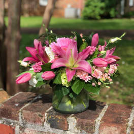 Pink lilies and mixed blooms arranged in a glass vase
