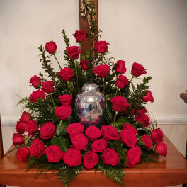 Large arrangement of red roses around a silver urn on a wooden table