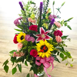 Mixed bouquet with sunflowers, roses, lilies, and a pink ribbon in a glass vase