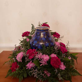 Pink flowers arranged around a blue decorative urn on a table