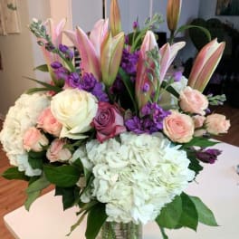 Bouquet of pink lilies, roses, hydrangeas, and purple flowers in a glass vase