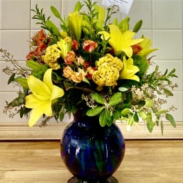 Yellow lilies and orange flowers arranged in a blue glass vase