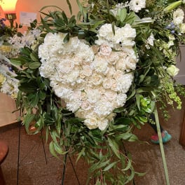 Heart-shaped white floral wreath on an easel with trailing greenery