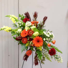 Tall mixed floral arrangement with orange gerberas and red blooms on a stand