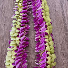 Two purple and pale green flower leis laid on a wooden surface