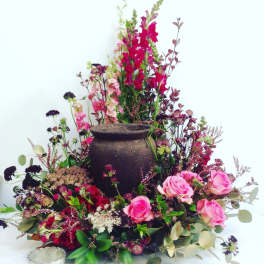 Pink roses and mixed flowers arranged around a dark urn centerpiece