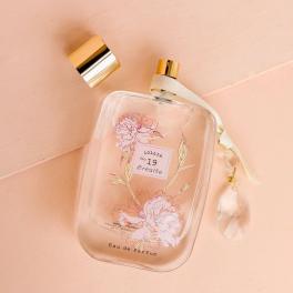 Clear perfume bottle with floral print and gold cap on a pink background