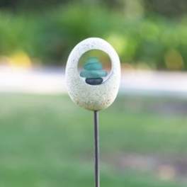 Small stone garden ornament on a metal stake with stacked blue pebbles
