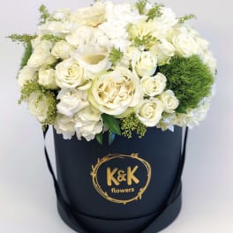 White rose arrangement in a black hatbox with gold logo