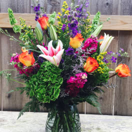 Colorful mixed bouquet in a glass vase with roses, lilies, and purple flowers
