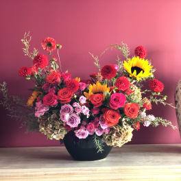 Mixed bouquet of red, pink, and yellow flowers in a black vase