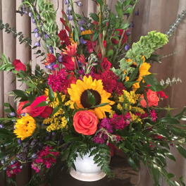 Tall mixed flower arrangement in a white vase with sunflowers and roses