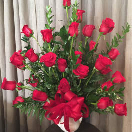 Red roses arranged in a white vase with a red ribbon bow