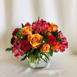 Mixed bouquet of orange roses, pink alstroemeria, and red blooms in a glass vase