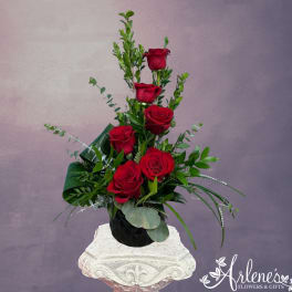 Tall arrangement of red roses in a black vase with greenery