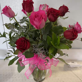 Bouquet of pink and red roses in a clear glass vase with a pink ribbon